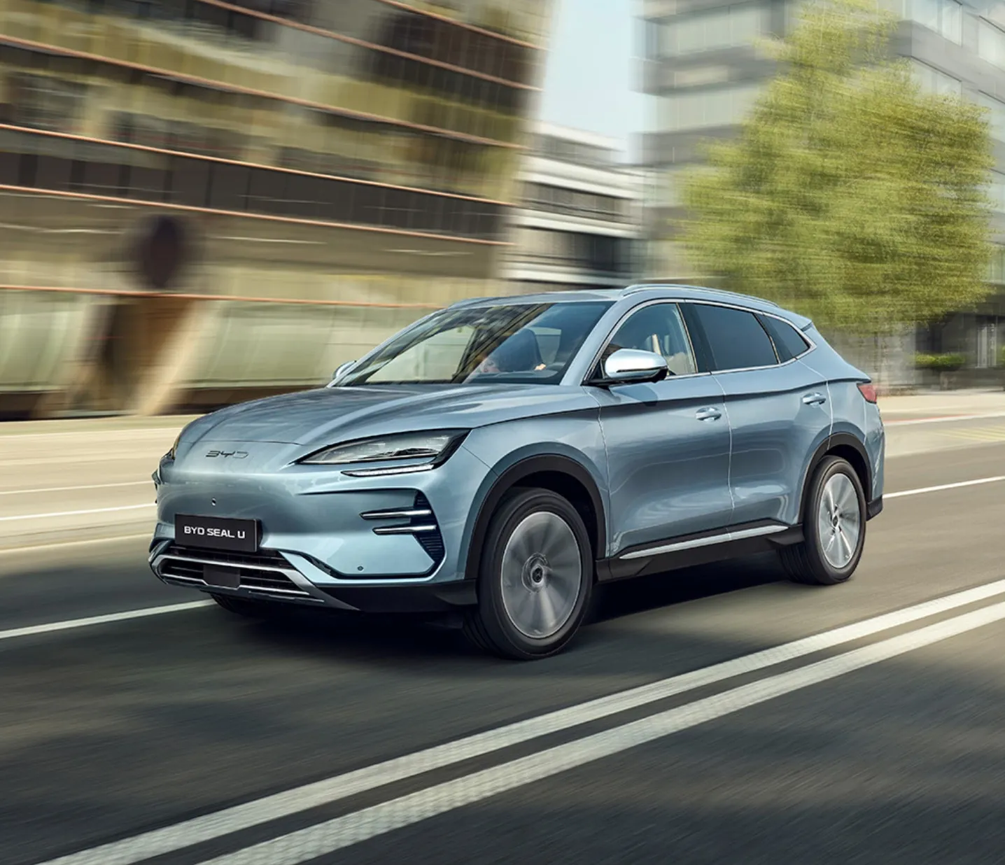 SUV elétrico BYD Seal U azul em movimento numa estrada urbana com edifícios modernos ao fundo.