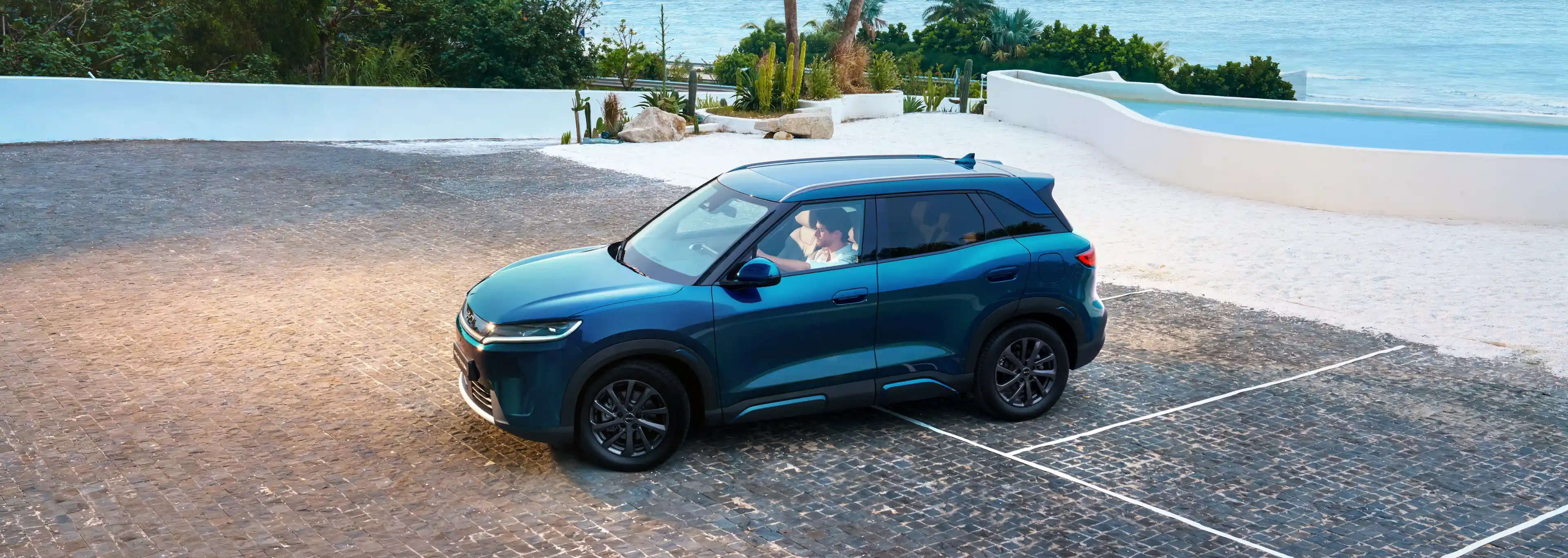 Imagem em ângulo elevado de um BYD ATTO 2 DM-i na cor azul, com jantes de liga leve escuras, numa área de estacionamento pavimentada.