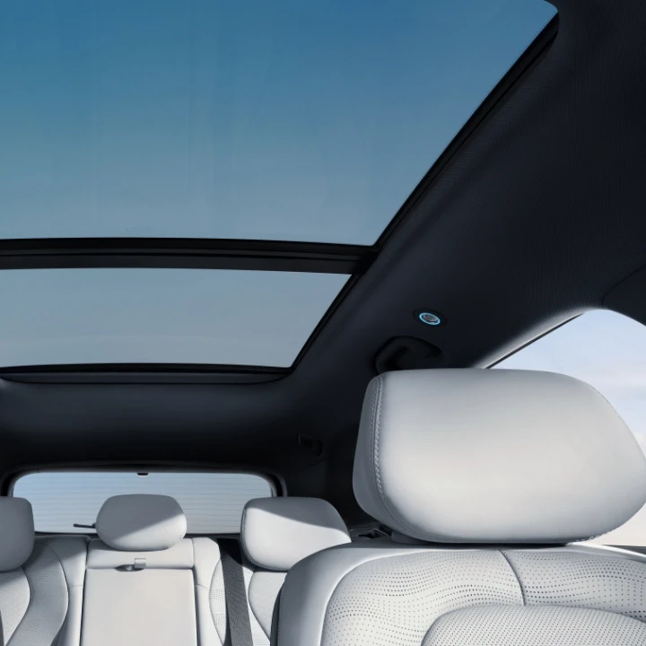 Vista do interior de automóvel destacando o teto de abrir panorâmico em vidro e os encostos de cabeça em estofos claros.