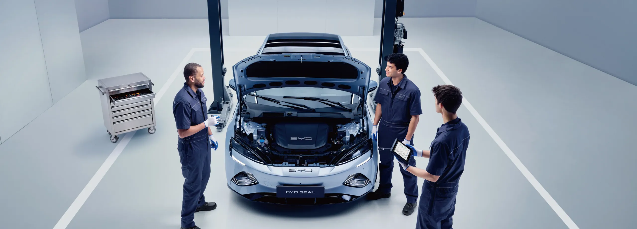 Três técnicos da BYD Service conversam ao pé de um BYD com o capot aberto