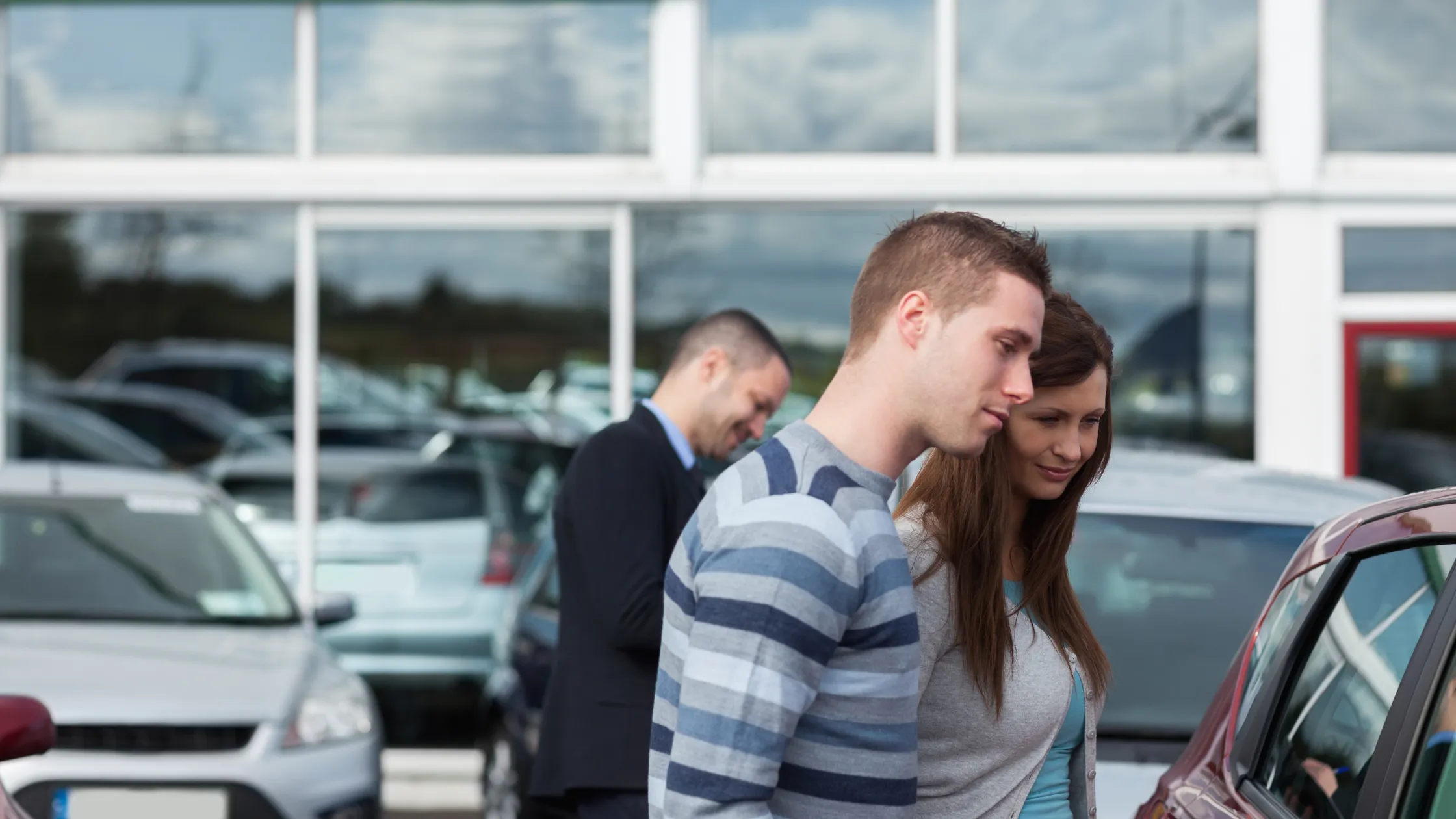 Pareja evaluando opciones en un concesionario antes de comprar un coche de segunda mano. Pareja en concesionario mira coches tras aprender como comprar un coche de segunda mano.