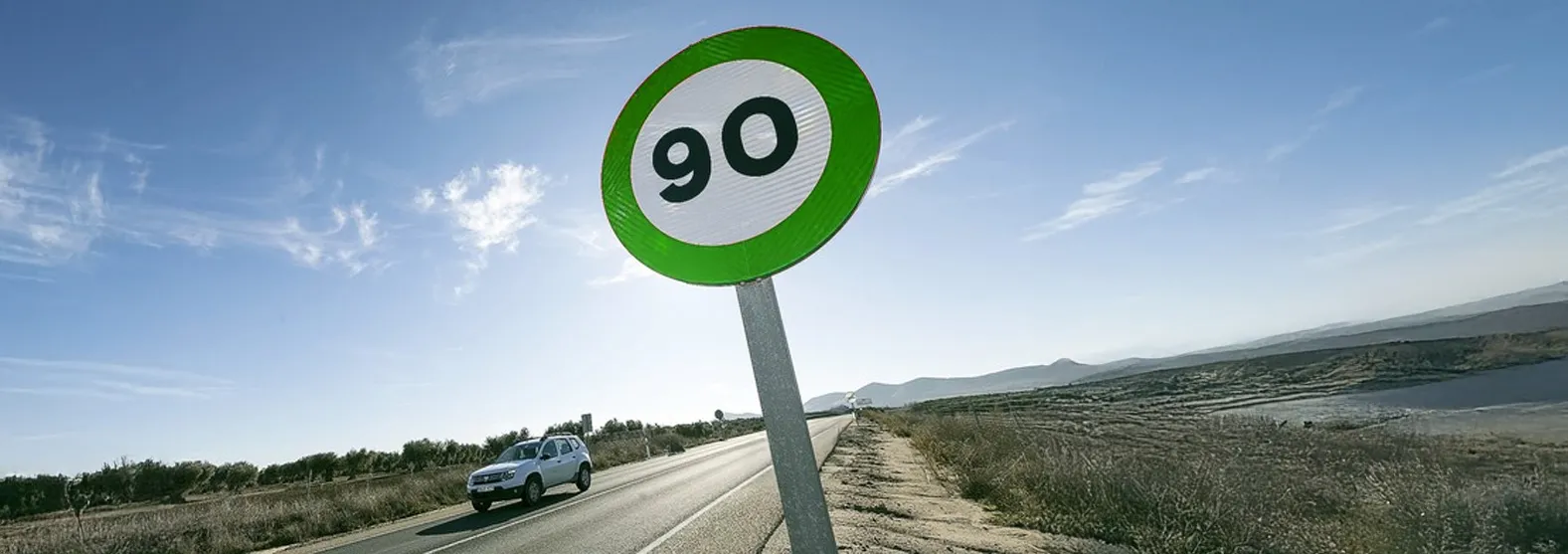 Señal de tráfico verde con límite de 90 km/h. Coche en ruta junto a señal de tráfico verde mostrando velocidad máxima de 90 km/h.