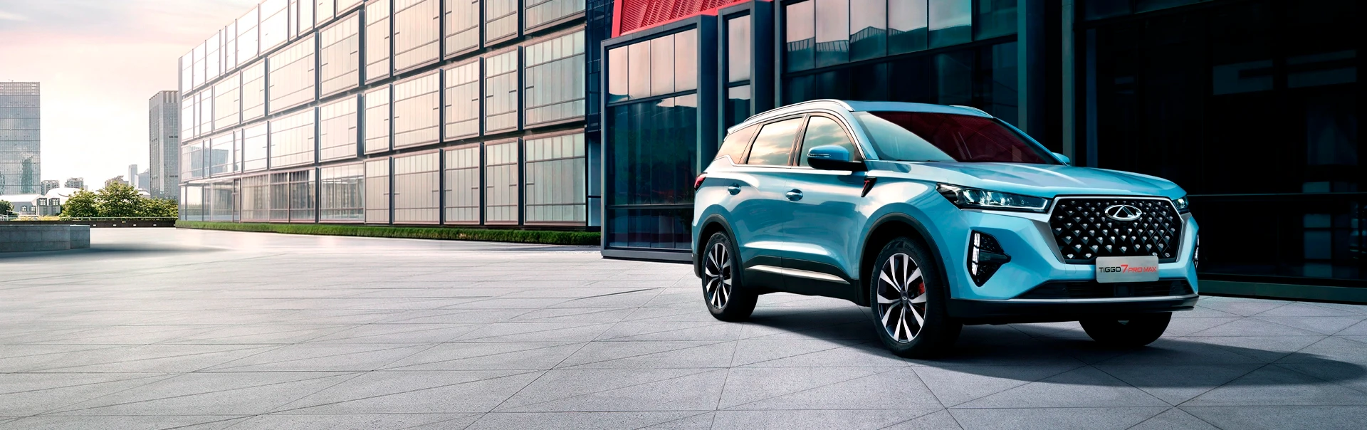 Chery Tiggo 2 azul estacionado em pátio moderno exterior com arquitetura urbana e janelas amplas.