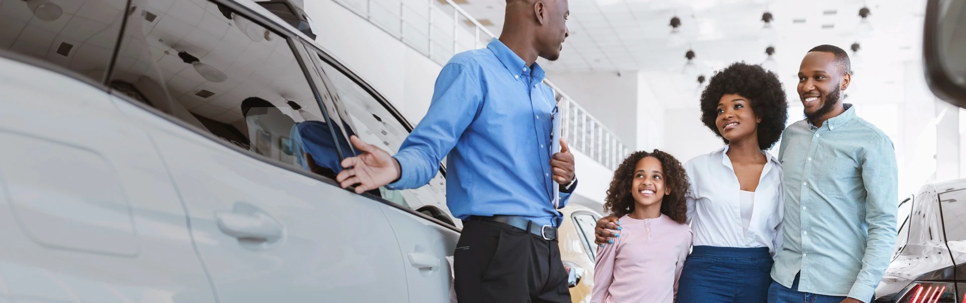 Consultor de vendas apresenta um carro novo a uma família sorridente num showroom moderno e luminoso.
