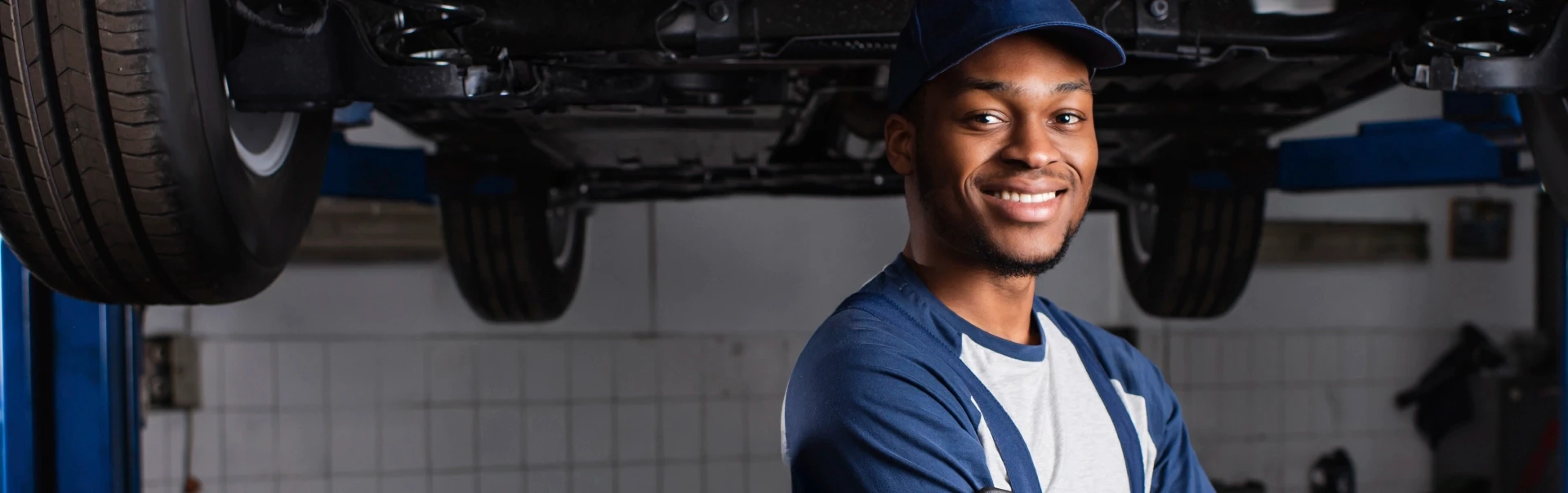 Professional mechanic in a blue uniform standing with arms crossed in a modern workshop with a vehicle on a lift