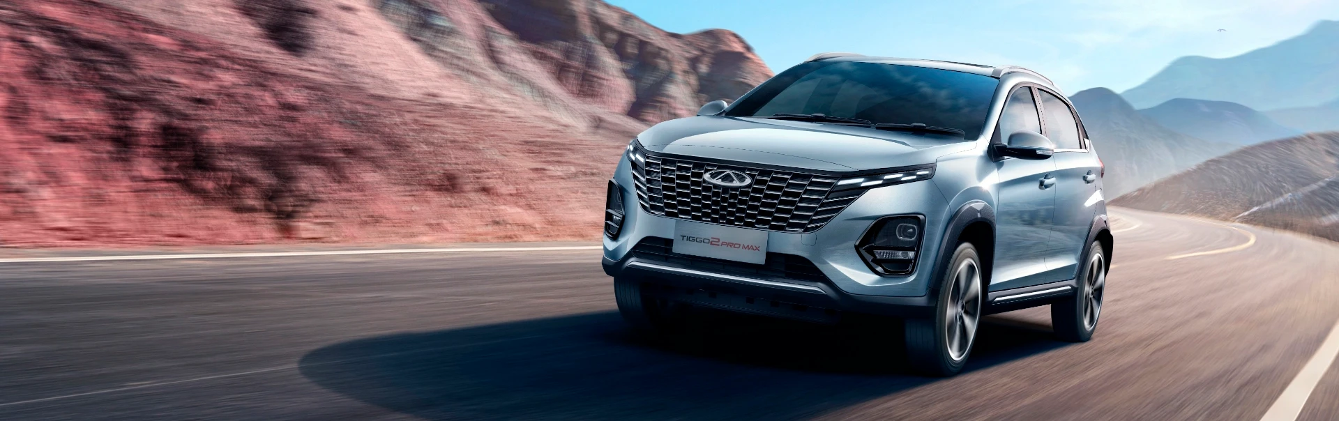 Tiggo 2 prateado em movimento numa estrada com um monte deserto por trás