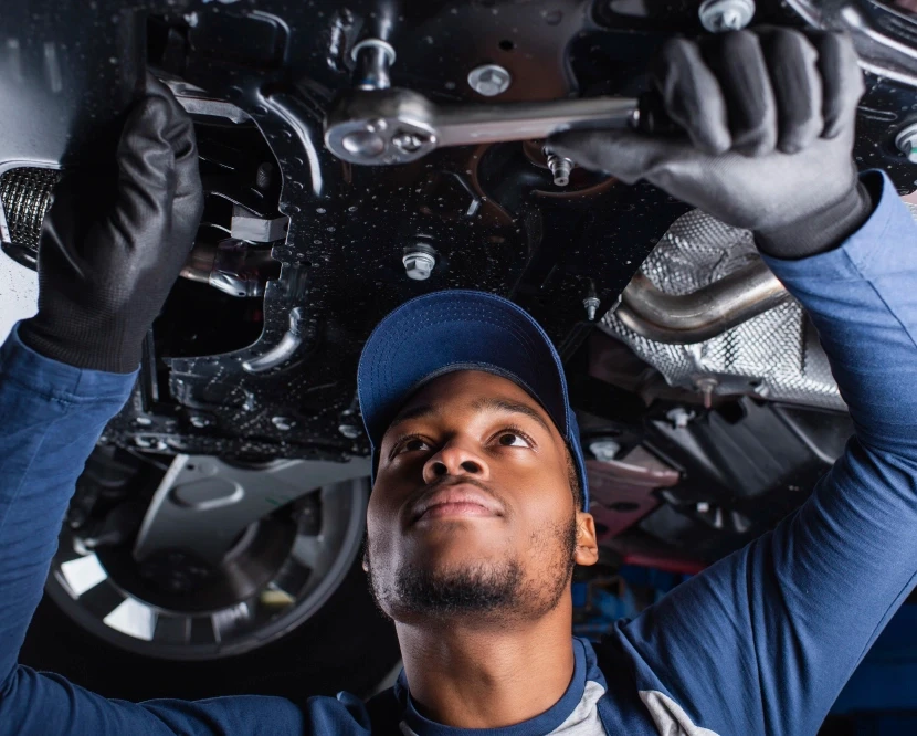 Professional automotive technician performing specialized underbody maintenance and technical inspection in a certified service center