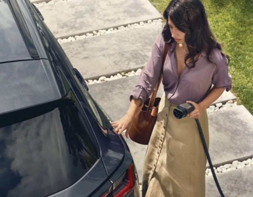 Mulher com carregador automóvel na mão, prestes a colocar um carro a carregar.