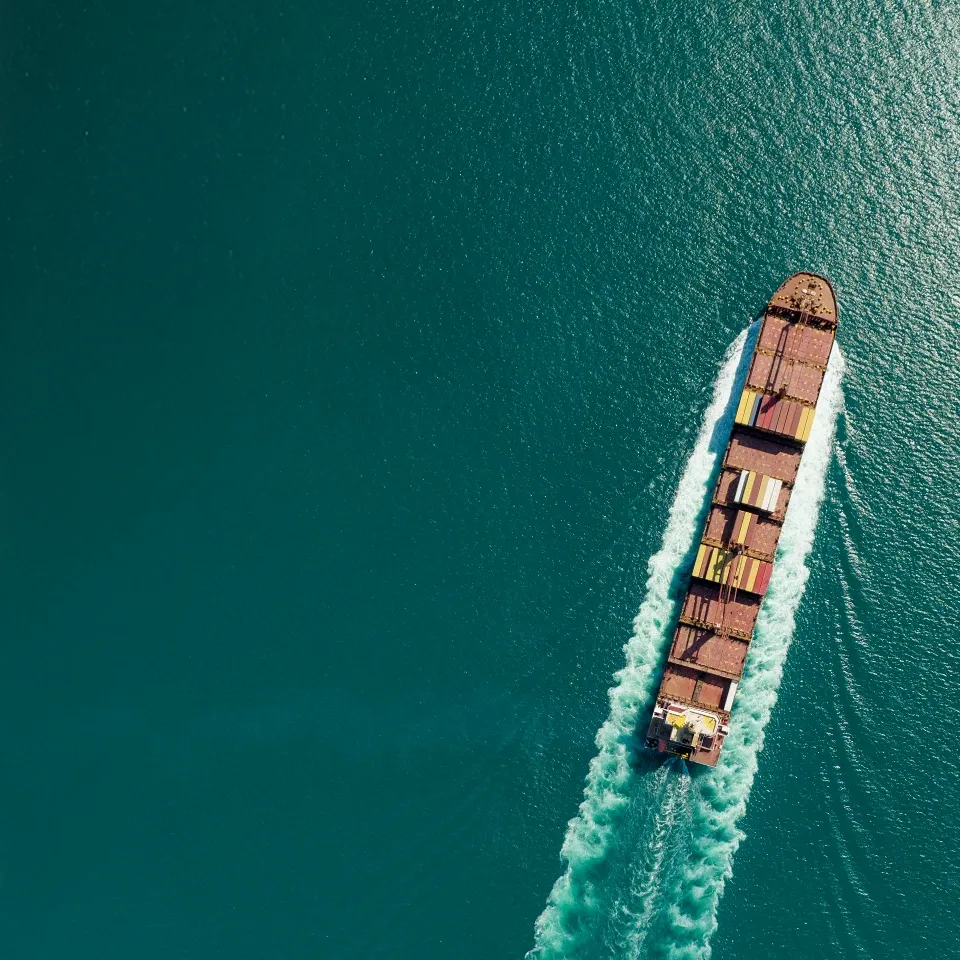 vista aérea de um navio com contentores no mar com águas verde-azuladas. 