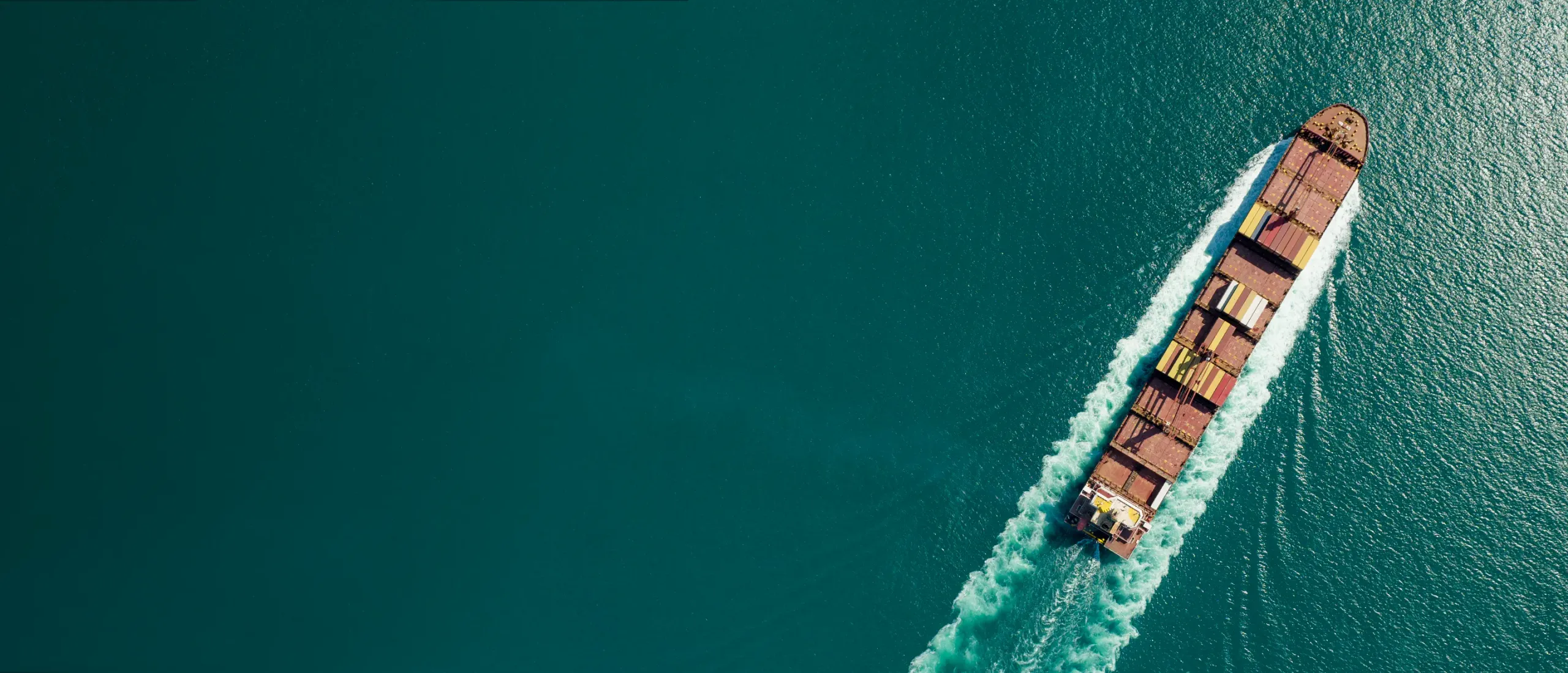 vista aérea de um navio com contentores no mar com águas verde-azuladas.