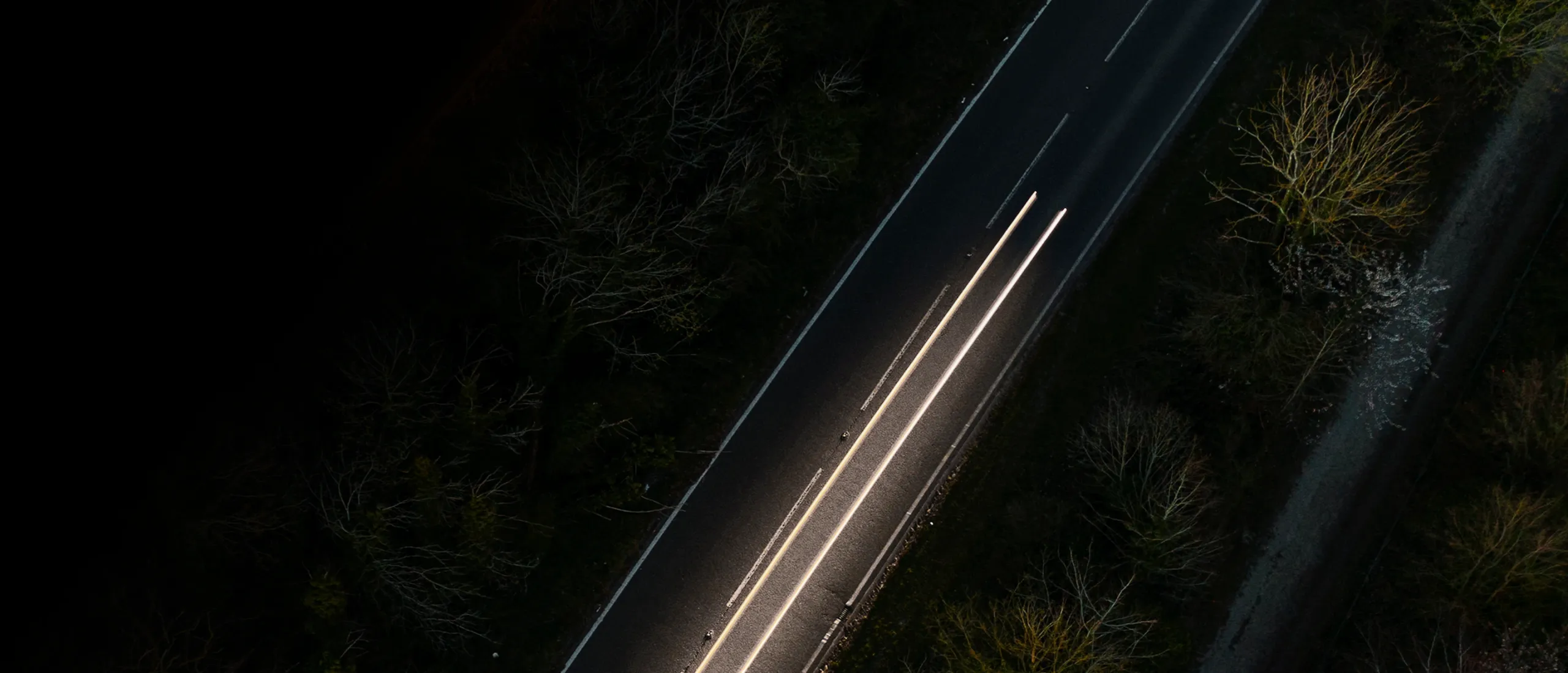 vista aérea noturna de uma estrada com rastos de faróis de um automóvel
