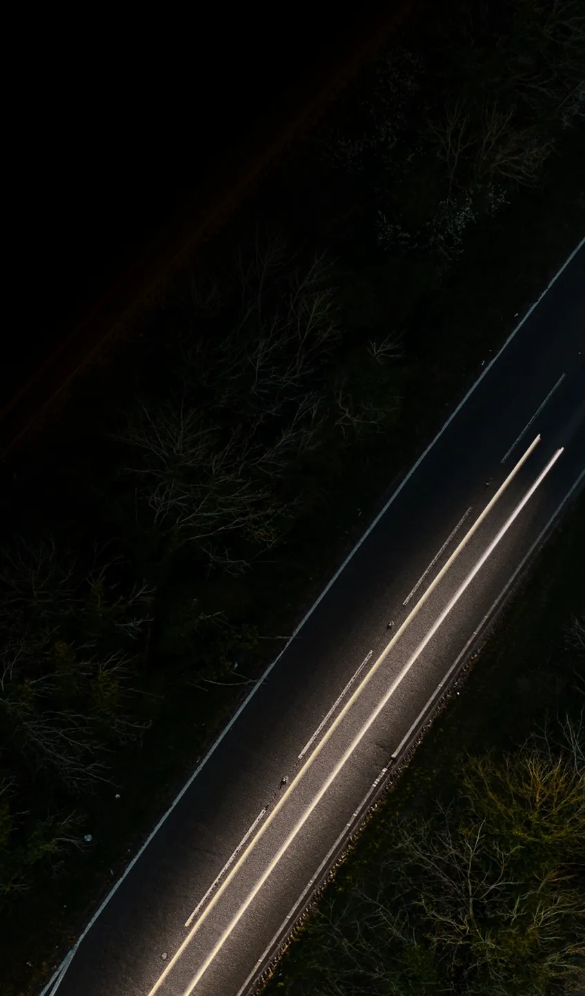 vista aérea noturna de uma estrada com rastos de faróis de um automóvel