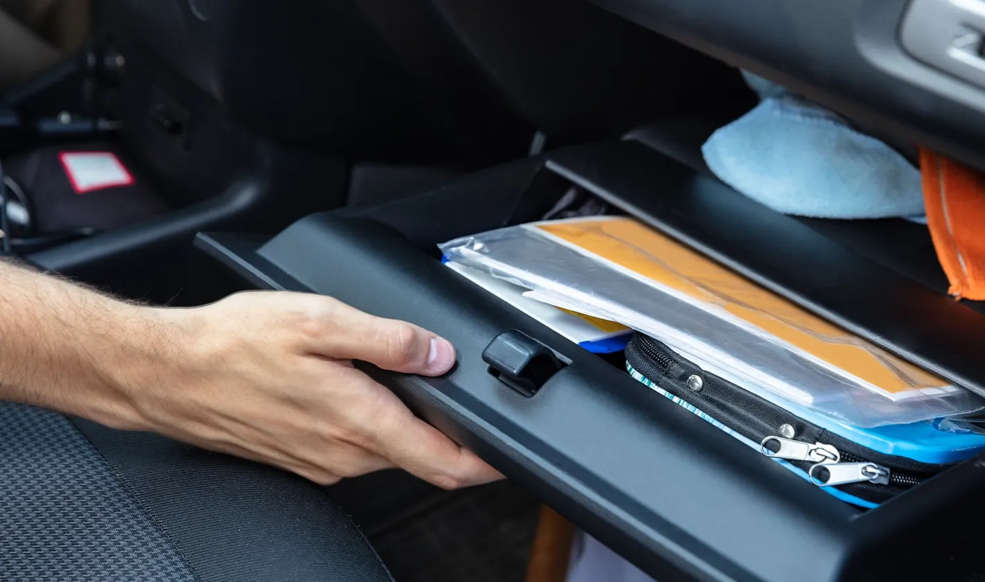 mão a abrir um porta-luvas de um carro com documentação no interior