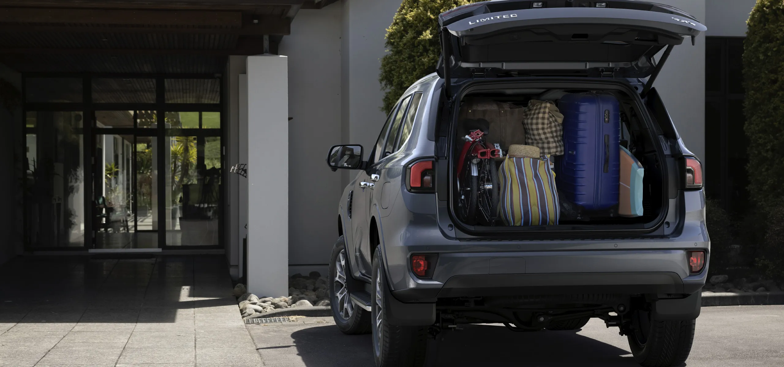 Ford Everest estacionada em frente a uma casa com o porta malas aberto e completamente cheio