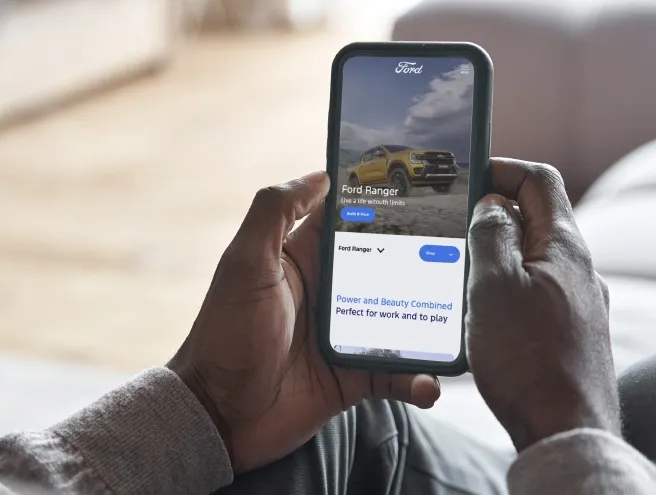 Une personne tenant un téléphone portable tout en regardant le nouveau site web de Ford