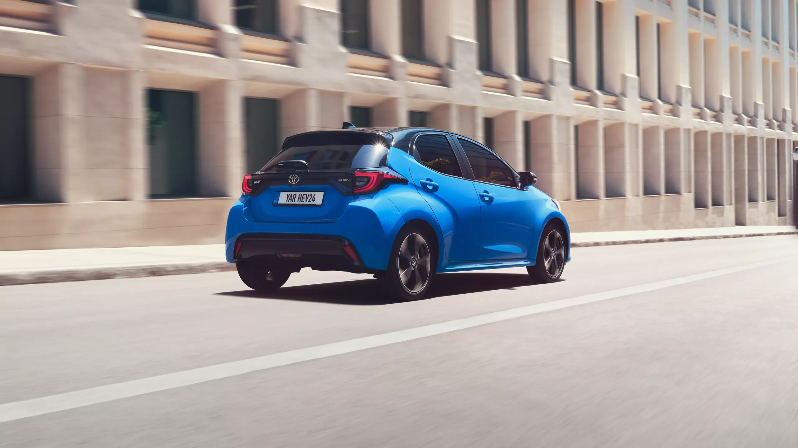 Toyota Yaris azul com vista frontal a circular ao lado de um grande edifício