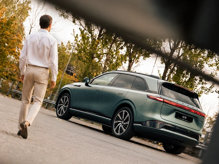 Empresário aproxima-se do SUV elétrico XPENG G9 verde, visto de traseira. 