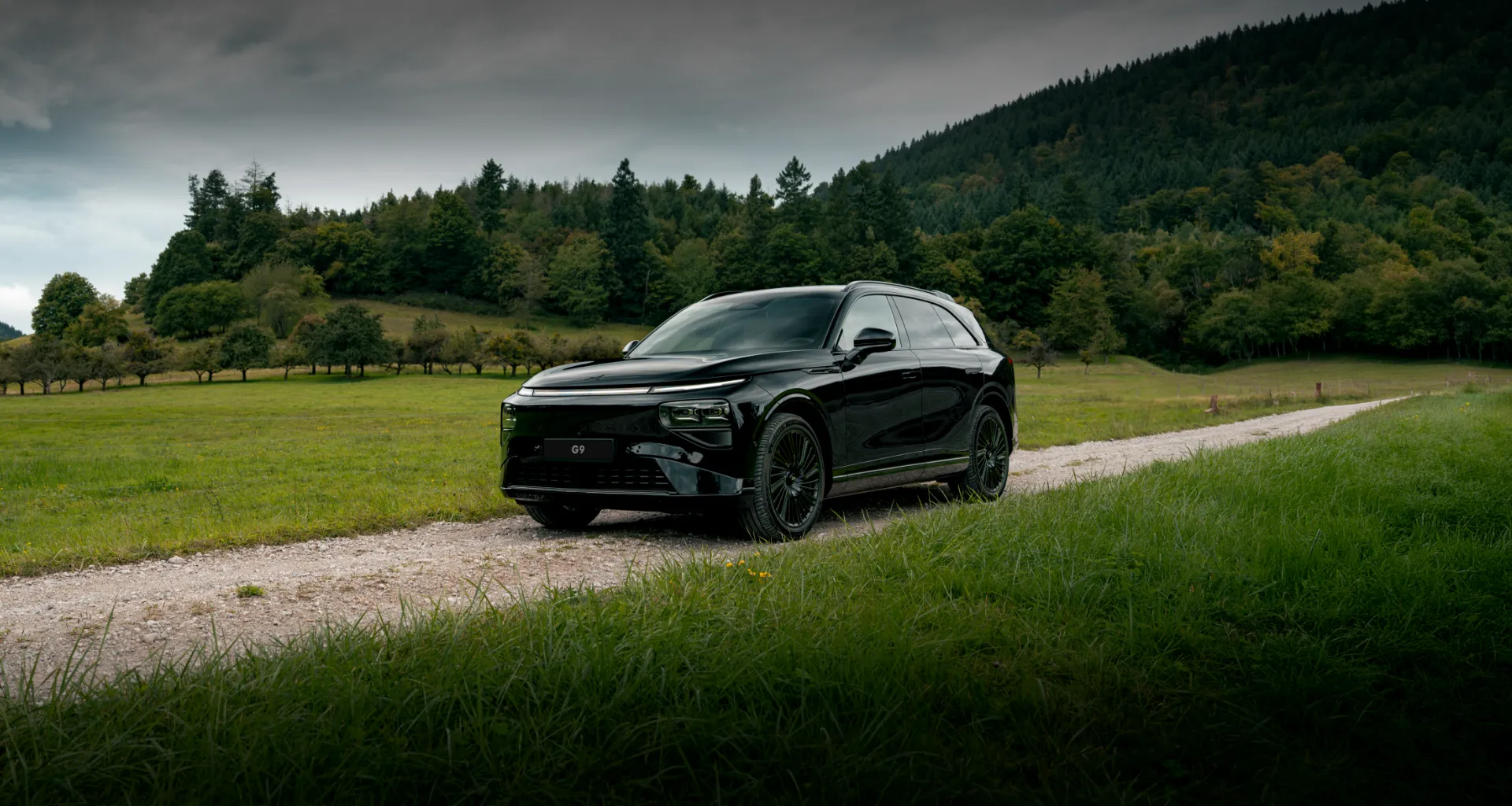 XPENG G9 na cor Midnight Black parado num caminho rural entre campos verdes.