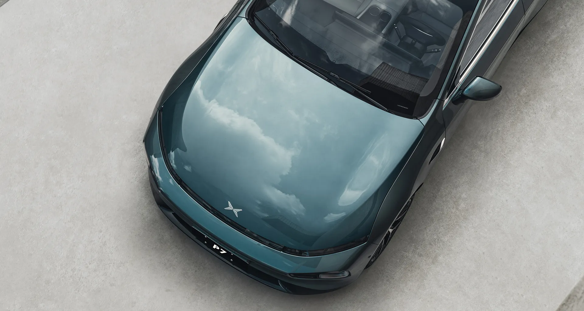 XPeng P7 de cor verde-azulado metálico visto de cima, refletindo nuvens no capô com design elegante e interior claro.